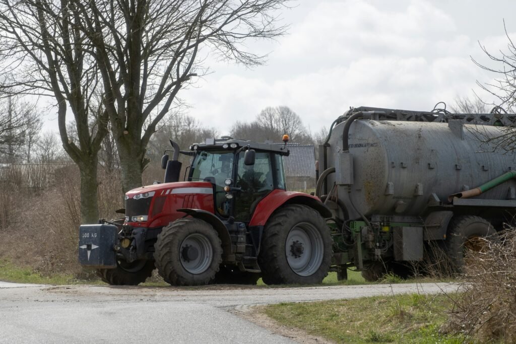Egy piros traktor kanyarodik az úton, mögötte egy nagy tartályos járművel.